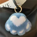 Detailed close-up of a blue and white fluffy cat paw charm on a black leather handbag - Blue