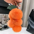 Dettaglio portachiavi a uva in finta pelliccia arancione con foglie su borsa in pelle - Arancione