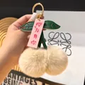 Detalle de llavero de cereza de peluche con pompones beige y hojas de cuero verdes - Color Té con Leche
