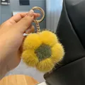 Close-up of plush yellow mink fur flower keychain with golden ring on black leather bag - Turmeric