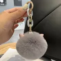 Detail of grey plush cat ear keychain with gold chain on a black leather handbag - Gray