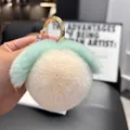 Close-up of peach-shaped fluffy plush keychain with gold clasp held in hand - Off White (Round Buckle)