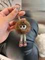 Close-up of a brown fluffy pompom keychain with big eyes, long legs and gold clasp - Brown