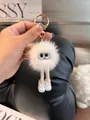 Close-up of white plush ball keychain with long legs and gold clasp on a magazine - White