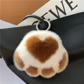 Plush cat paw keychain with brown heart detail and golden ring on a black leather bag - White + Caramel