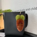 Detailansicht eines Plüsch-Karotten-Anhängers mit Goldhaken an einer schwarzen Handtasche - Klassisches Kaffee
