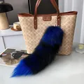 Detail of blue and black striped faux fur fox tail charm with gold metal clasp on a bag - Blue