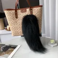 Close-up of black fluffy fur tail keychain with gold clasp on a brown handbag - Black