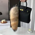 Lush faux fur fox tail bag charm with golden metal clasp on a textured leather handbag - Wolf Tail Color