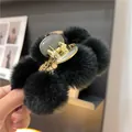 Close-up of fluffy black faux fur pom-poms on a gold hair claw clip for winter styling - Black