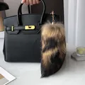 Detail of real fox fur tail charm with gold chain on black leather handbag - Raccoon Dog Tail Color