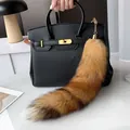 Detail of fluffy brown fox tail keychain attached to black leather handbag with gold hardware - Small Red Fox