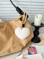 Close-up of white heart-shaped plush keychain on a khaki suede bag with braided strap - Beige