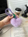 Detail of a purple fluffy heart keychain with a woven strap held in a cozy home setting - Purple