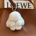 White mink fur bunny keychain with golden ring attached to a brown leather bag - Cross Mink Leather Paws