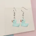 Close-up of light blue resin duck earrings on a display stand with a soft pastel background - Blue
