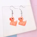 Close-up of orange-pink resin duck earrings with silver hooks on transparent display - Orange