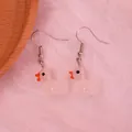 Macro detail of cute white resin duck earrings with orange beaks and silver hooks - Luminous Milky White