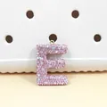 Gros plan détaillé du pendentif lettre E en strass rose avec anneau doré et effet brillant - Lettre E en Strass Rose (E)