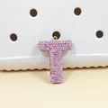 Charm lettre T en strass rose pour sabots présenté sur un fond blanc texturé à trous - Lettre T en Strass Rose (T)