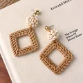 Nahaufnahme von gewebten Boho-Rattan-Ohrringen mit weißen Perlen auf einem Buch - Quadratische Rattan-Ohrringe mit weißem Perlencluster (28218D)