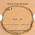Detail view of gold Morse code beads spelling Fuck Off on a brown kraft card display - Gold (Fuck Off)
