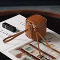 Braune Mini-Zylinder-Kosmetiktasche aus Leder mit goldfarbenem Reißverschluss und Gurt - Braun