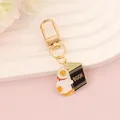 Detail of a cartoon cat enamel keychain holding a book with gold lobster clasp - Cat Burying Head in Book