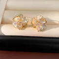 Primer plano detallado de pendientes de botón de flor dorados con piedras de circón brillantes - Tops / Dorado
