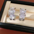 Macro view of C-shaped earrings featuring wrinkled flowers and sparkling zircons. - Pleated Flower Shape / Silver