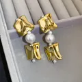 Nahaufnahme von unregelmäßigen goldenen geometrischen Ohrringen mit weißen Perlen - Ohrringe (Stahl-Ohrstecker) / Gold/Weiß
