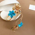 Close-up of golden spiral arm cuff featuring vibrant blue enamel flowers and metal petals - Blue