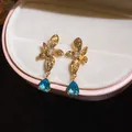 Close-up of 18k gold plated floral stud earrings with blue teardrop zircon details - Hollow Flower Teardrop Style (HE33127) / Gold with Blue