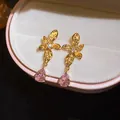 Detailed macro view of floral stud earrings with pink teardrop zircon in a jewelry box - Hollow Flower Teardrop Style (HE33127) / Gold Plated Pink