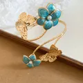 Close-up van de elegante gouden armband met vlinder en blauwe emaille bloemdetails. - Blauw