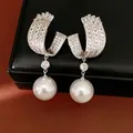 Close-up detail of silver U-shaped earrings with cubic zirconia and pearl drops - Silver
