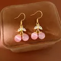 Close-up of elegant gold plated cherry earrings with pink cat's eye stones and zircons. - Hook Style / Pink