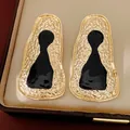 Primo piano di orecchini dorati geometrici irregolari con dettaglio in smalto nero elegante - Oro Nero