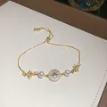 Dettaglio di un braccialetto dorato con pavé di zirconi, perle bianche e ciondoli a stella - Stile Stella e Luna 1#