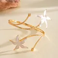 Détail d'un élégant bracelet de bras doré avec des étoiles de mer en émail - Blanc