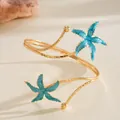 Vue détaillée d'un bracelet de bras doré avec des étoiles de mer en émail bleu plage - Bleu