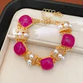 Vista detallada de una elegante pulsera vintage dorada con piedras fucsia y perlas - Pulsera / Dorado-Púrpura