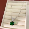 Detailed close-up of V-letter necklace with a large round green gemstone in a jewelry box - Silver/Green
