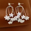 Dettaglio di orecchini pendenti in argento con delicati fiori di resina bianca e zirconi - Bianco