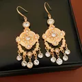 Gros plan détaillé de boucles d'oreilles vintage dorées évidées avec des strass étincelants. - Crochets de boucles d'oreilles / Or