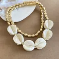 Primer plano de un collar bohemio de dos capas con cuentas doradas y dijes de acrílico. - Collar / Caqui