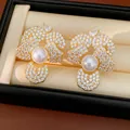 Close-up detail of elegant gold flower earrings with pearls and CZ stones in box. - Gold