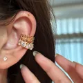 Primo piano di un elegante ear cuff dorato con motivi a stella e zirconi tondi. - Orecchini a clip / Oro