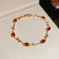 Close-up detail of a gold vine bracelet featuring red oval zircons and green leaves - Red & Green Vine / Gold