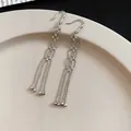 Close-up of elegant silver tassel earrings with zircon studs on a beige plate - Silver